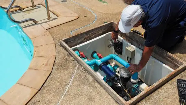 Technician checking circulation equipment beside a swimming pool
